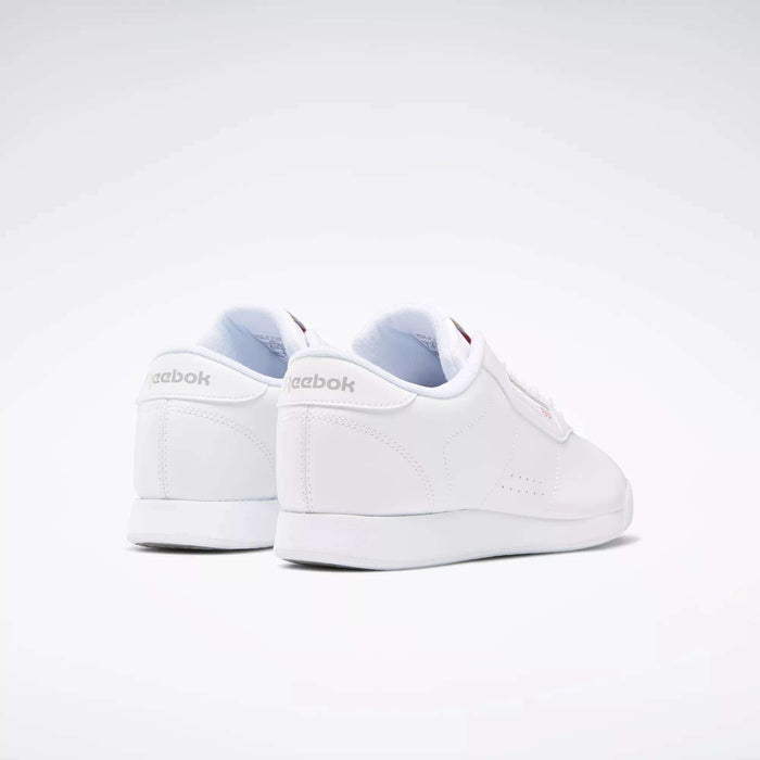The Reebok Women's Princess Wide Shoes are shown from the back and side against a light background, featuring subtle stitching, a heritage cushion sole, and Reebok logos with Union Jack detail on the heel and side.