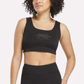 A woman wearing a black Women's Reebok x F45 Training Sports Bra stands against a plain light background.