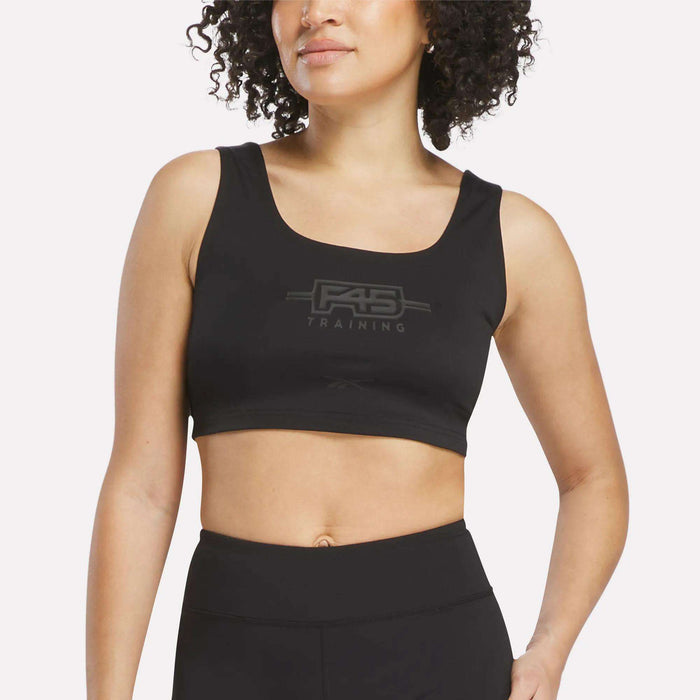 A woman wearing a black Women's Reebok x F45 Training Sports Bra stands against a plain light background.