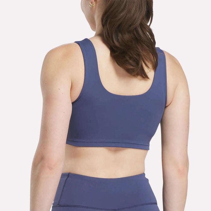 A woman with brown hair in a ponytail is shown from the back, wearing the Women's Reebok x F45 Training Sports Bra in blue. The background is plain white.