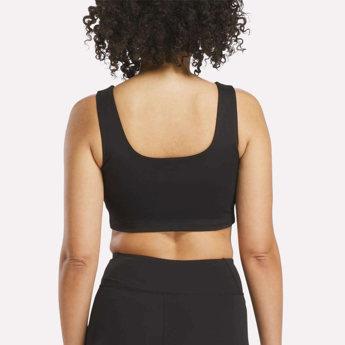 A person with curly hair is shown from the back, wearing a black Women's Reebok x F45 Training Sports Bra and black high-waisted leggings against a plain white background.