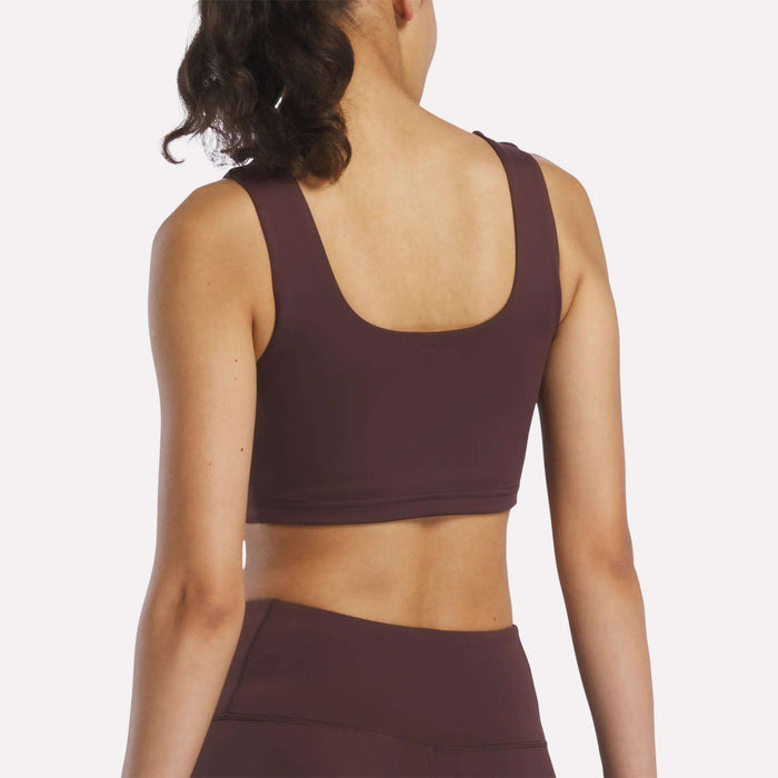 A woman with curly hair in a ponytail is shown from the back wearing the Women's Reebok x F45 Training Sports Bra and matching high-waisted leggings, perfect for an F45 Training session, against a plain light background.