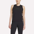A woman stands with arms relaxed by her sides, wearing a sleeveless black Reebok x F45 Training Tank Top and black leggings. The sweat-wicking top is perfect for high-intensity workouts, shown against a plain light background.
