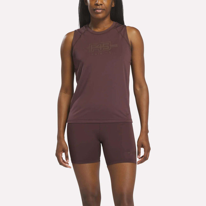 A woman stands facing forward wearing the Women's Reebok x F45 Training Tank Top in Dark Cocoa, paired with matching shorts. This sleeveless Reebok athletic top features sweat-wicking fabric, making it ideal for F45 Training sessions. The background is plain white.
