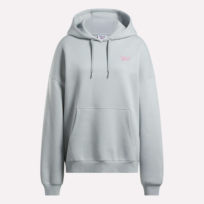 The Reebok Women's Relaxed Fleece Hoodie is an oversized light gray hoodie featuring a front pocket, drawstring hood, and a small pink Reebok logo on the left chest. It is shown against a plain white background.