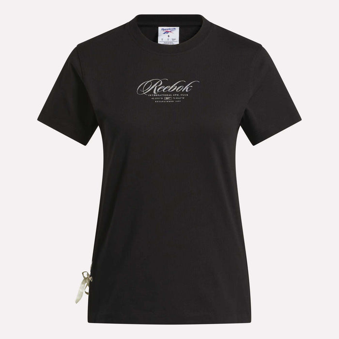 The Reebok Women's Ribbon T-Shirt is shown in black with short sleeves against a white background. It features the brand’s cursive logo on the chest and a small ribbon detail at the bottom left hem. Made from soft cotton, this t-shirt offers comfortable wear and metallic shine for a stylish everyday look.