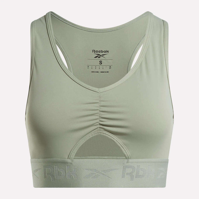 The Women's Ruched Sports Bra by Reebok comes in light green and features a racerback design with a ruched front. Designed for medium-impact activities, it includes performance technology for added comfort, a wide elastic band at the bottom with the Rbk logo, and a visible inner label at the back.