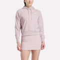 A person wearing a light pink Women's Small Vector Cropped Hoodie by Reebok with a front pocket and matching fitted skirt, standing against a plain white background.
