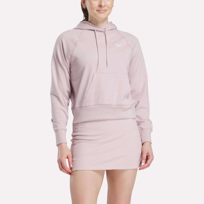 A person wearing a light pink Women's Small Vector Cropped Hoodie by Reebok with a front pocket and matching fitted skirt, standing against a plain white background.