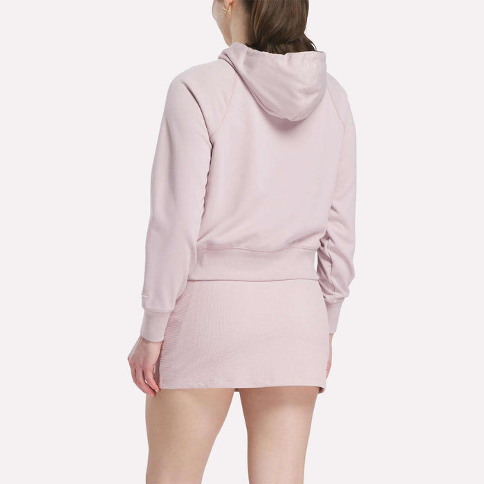 A person is shown from the back, against a plain white background, wearing a light pink Reebok Women's Small Vector Cropped Hoodie with a matching mini skirt.