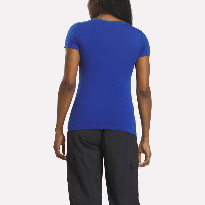 A woman is seen from behind wearing a fitted Reebok Women's T-Shirt (short sleeves, royal blue) with black pants, set against a plain white background.