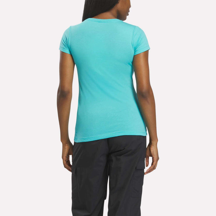 A person with long hair is seen from behind, wearing a fitted Reebok Women's T-Shirt and black pants against a plain, light background.