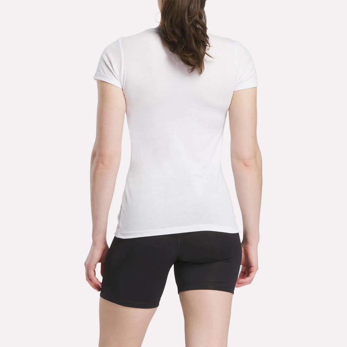 A person with long brown hair is seen from the back, wearing a fitted Women's Reebok T-Shirt and black shorts, standing against a plain white background.