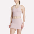 A woman in a light pink Women's Time Out Cropped Tank Top by Reebok and a matching high-waisted mini skirt stands against a plain white background, smiling slightly.
