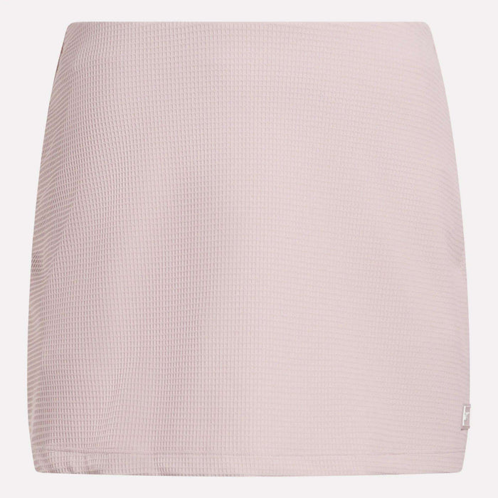 The Reebok Women's Time Out Slim Tennis Skort features a light pink, waffle-textured fabric and straight cut—a minimal design ideal for sporty flair in your activewear wardrobe. Shown against a white background.