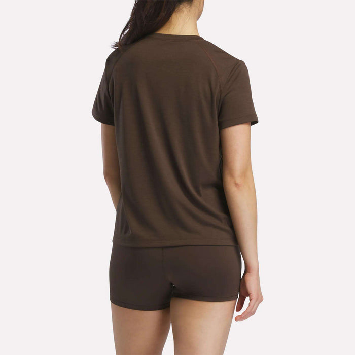 A woman faces away from the camera, wearing a brown Reebok Women's Training T-Shirt and matching shorts against a plain white background.
