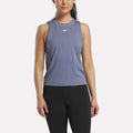 A woman in a blue Reebok Women’s Training Tank Top with RBK-DRY technology and black leggings stands facing forward against a white background. The tank has a small white logo on the chest.