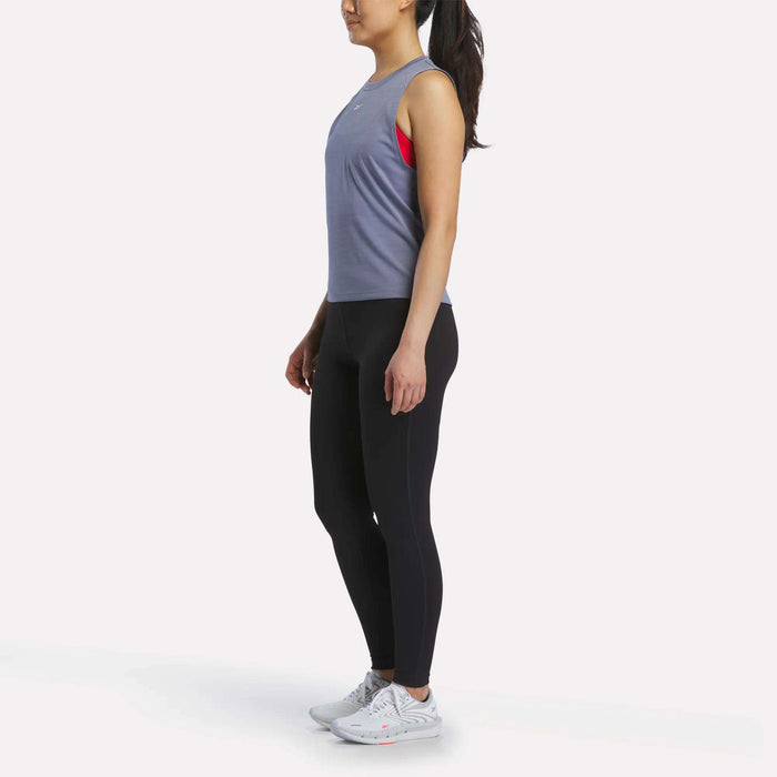 A woman poses against a plain white background in Reebok athletic wear, featuring the Women's Training Tank Top in sleeveless lavender, paired with black leggings and white sneakers.