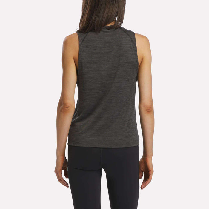A woman with long brown hair is seen from behind, wearing a sleeveless Reebok Women's Training Tank Top in dark gray paired with black leggings, standing against a plain white background.