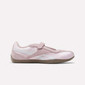 The Reebok Women's Ultra Lo Mary Jane Shoes are light pink with white accents, a suede finish, velcro strap, and tan rubber sole, shown in profile on a plain white background.
