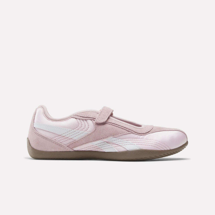 The Reebok Women's Ultra Lo Mary Jane Shoes are light pink with white accents, a suede finish, velcro strap, and tan rubber sole, shown in profile on a plain white background.