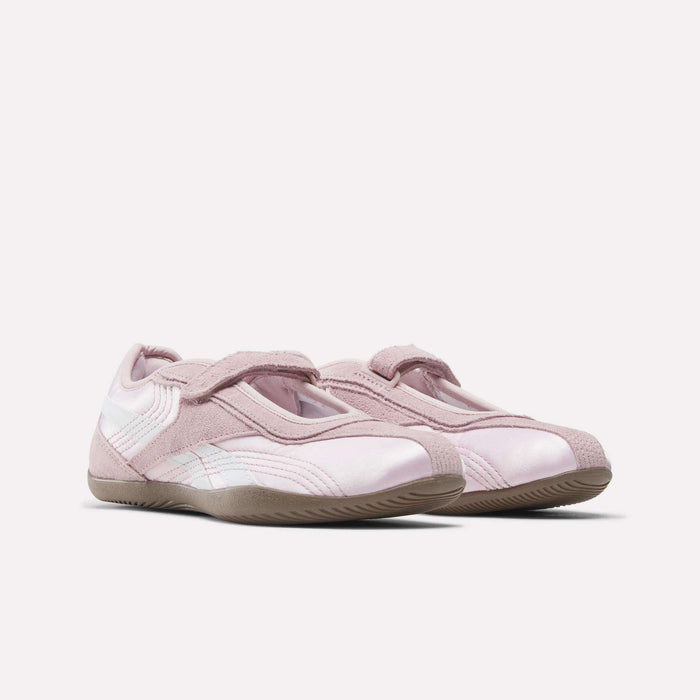 The Women's Ultra Lo Mary Jane Shoes by Reebok feature a light pink low-profile runner style with suede and mesh accents, velcro straps, and textured rubber soles, shown on a plain white background.