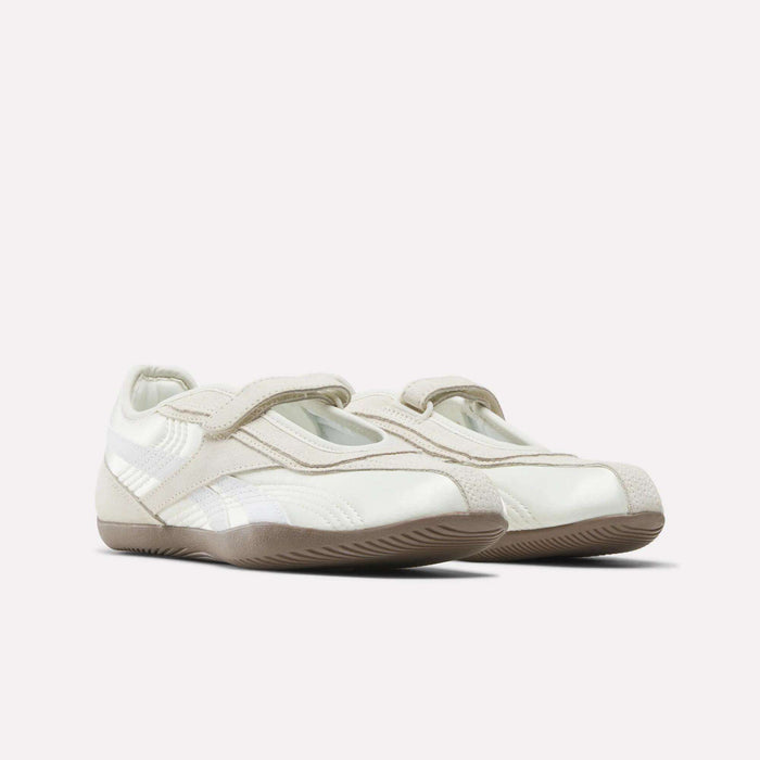 The Reebok Women's Ultra Lo Mary Jane Shoes feature a white and beige low-profile runner design with Velcro straps and subtle stitching details, displayed on a plain light background.