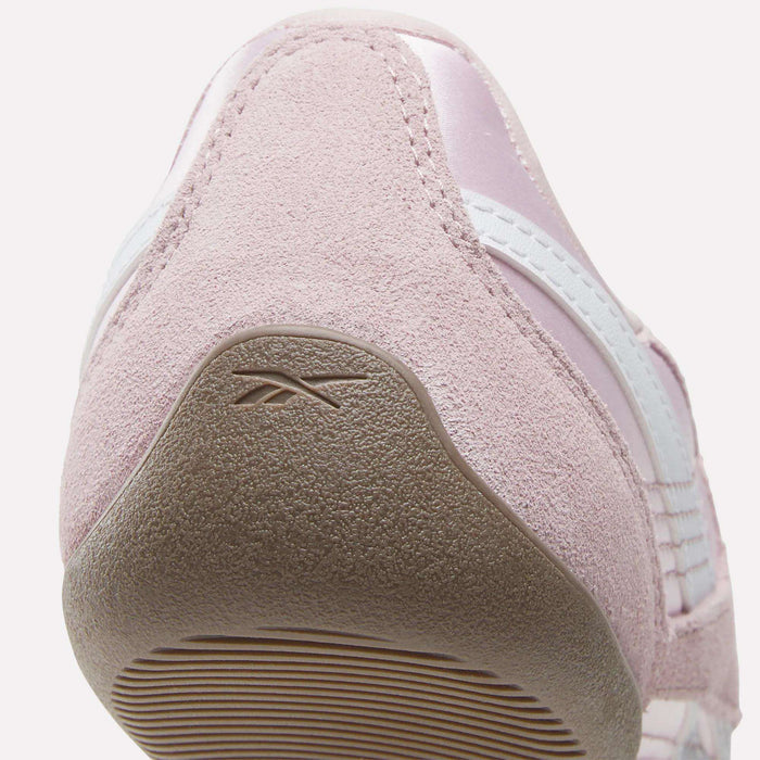 Close-up view of the heel of a light pink Women's Ultra Lo Mary Jane Shoe by Reebok, featuring a textured suede finish, white stripes, and the Reebok logo embossed on the heel section of the rubber outsole.