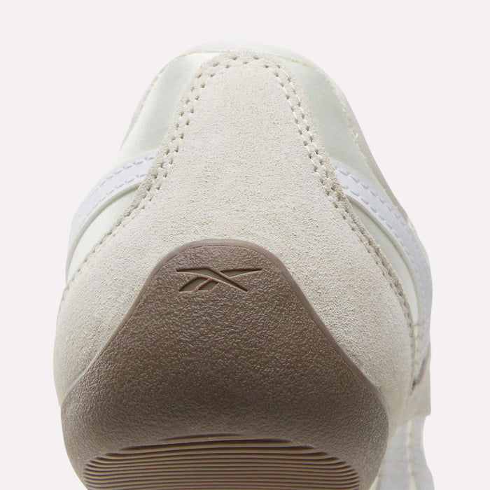 Rear view of a beige suede Women's Ultra Lo Mary Jane Shoe by Reebok, featuring a light brown textured heel with an embossed logo, white stitching, and a partial white side stripe.