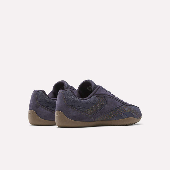 A pair of Reebok Women's Ultra Lo Shoes in dark purple suede, showcasing brown stitched accents and textured gum soles, is displayed from the back and side against a plain white background.