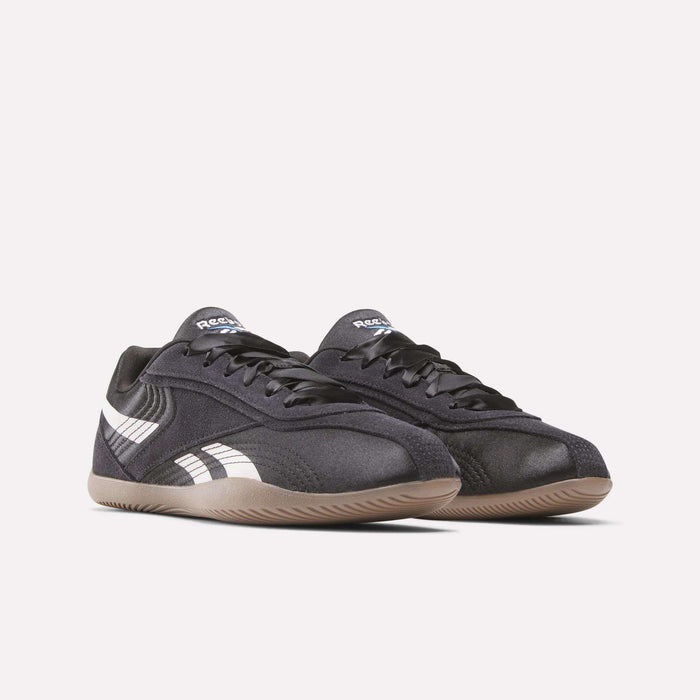 A pair of Women's Ultra Lo Shoes by Reebok in black with white side stripes, black laces, and light brown rubber soles, shown on a plain white background. Sport-inspired style for any outfit.