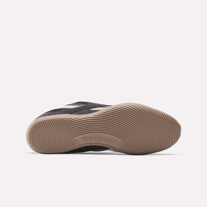 A black Reebok Women's Ultra Lo Shoe is shown on its side, highlighting its light brown textured rubber sole with the Reebok logo and white stripes, featuring a sport-inspired style.