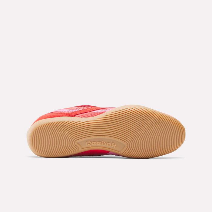 A Reebok Women’s Ultra Lo Shoe in red lies on its side, highlighting the textured tan rubber sole with a wavy grip pattern and the Reebok logo—ideal for sport-inspired, low-profile women’s style.