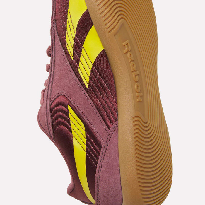A close-up of Reebok Women's Ultra Lo Shoes in maroon with yellow stripes and a brown rubber sole, highlighting the side and bottom details against a white background.