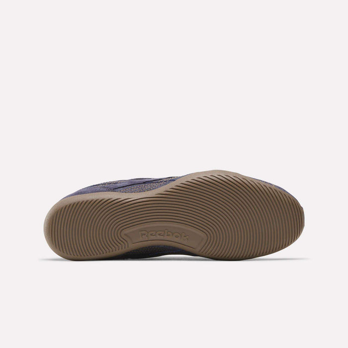 A close-up of the bottom of the Reebok Women's Ultra Lo Shoes showcases a tan rubber sole with textured, wavy grip patterns and the embossed Reebok logo at the center. The upper part of this shoe features a dark color reminiscent of dark wash denim.