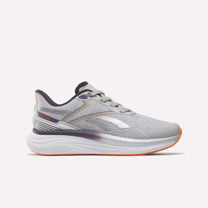 The Women's Viva Speed Shoes by Reebok feature a New Grey 1 upper with Phantom Purple and Alt Orange accents. Designed for both style and support, these athletic running shoes showcase the iconic Reebok logo on the side. A thick, white cushioned midsole provides superior comfort, while the shoes are photographed against a plain white background.