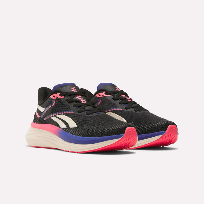 The Reebok Women's Viva Speed Shoes are black with white and pink accents, a breathable upper, black laces, extra cushioning, and white soles featuring a gradient pink-to-purple midsole, displayed on a plain white background.