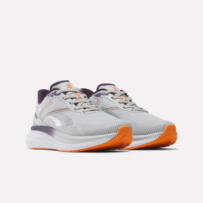 The Women's Viva Speed Shoes by Reebok are shown on a plain white background. This pair features a light gray color with white and orange accents, purple inner lining, and orange soles. Designed for all-day comfort, these breathable shoes offer a cushioned design perfect for everyday wear.