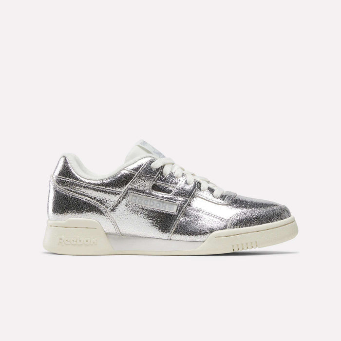 A pair of Reebok Women’s Workout Plus Shoes in Silver Metallic/Chalk/Vintage Chalk, crafted from premium garment leather with matching white laces and chalk-toned sole, shown from a side angle against a plain white background for a classic sneaker aesthetic.