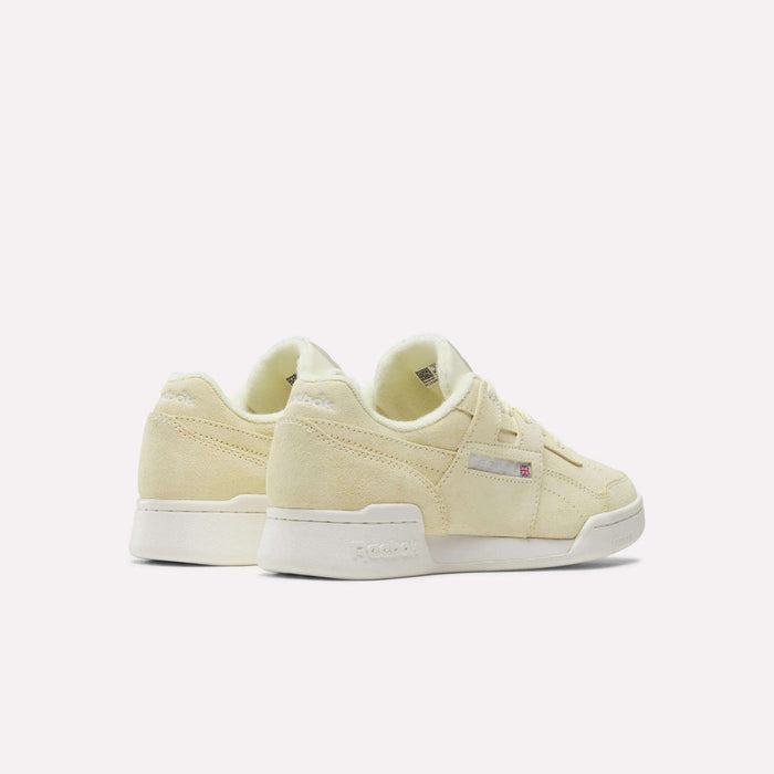 A pair of Women's Workout Plus Shoes by Reebok in light yellow suede with white soles, shown from the back and side on a white background. Classic '80s fitness style and subtle branding complete these women's sneakers.