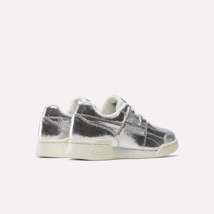 A pair of Reebok Women’s Workout Plus Shoes in silver metallic, made from premium garment leather, featuring white laces and off-white soles, displayed against a plain light background.