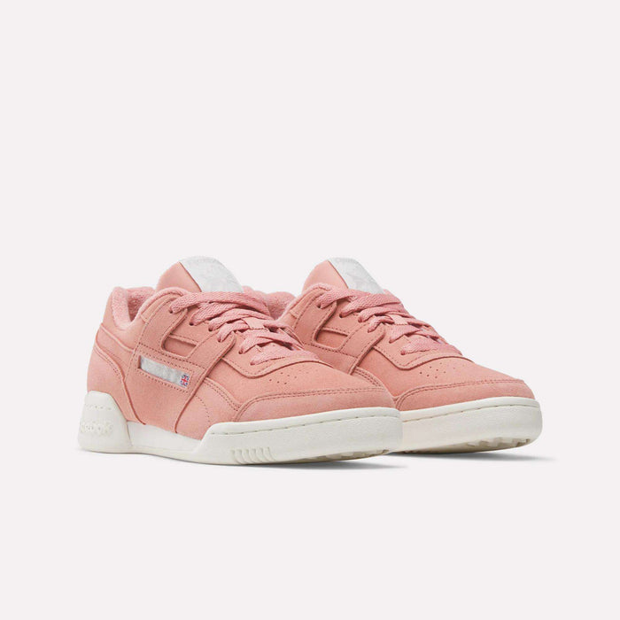 The Reebok Women's Workout Plus Shoes are pink low-top sneakers with white soles and laces, inspired by authentic 80s fitness style, featuring subtle stitching details. Displayed on a plain white background.