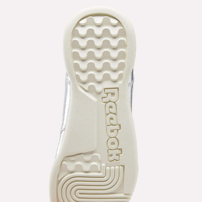 Certainly! Here’s a revised version of your sentence using the provided product data: The sole of a Reebok Women’s Workout Plus Shoe in white, viewed from below, displays the distinctive wavy tread pattern and the prominent raised Reebok logo at the center—an iconic sneaker designed with premium garment leather for enduring style and durability.