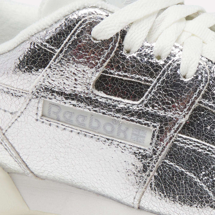 Close-up of a silver cracked-leather Reebok Women’s Workout Plus Shoe with white laces, crafted from premium garment leather. The Reebok logo is visible on the side of this classic sneaker, inspired by the iconic Workout Plus design.