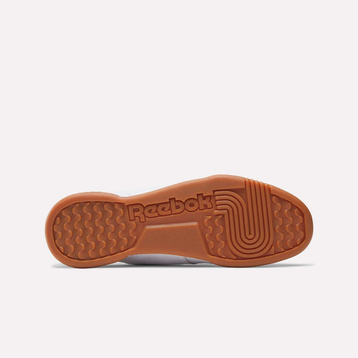 The image displays the sole of the Reebok Women's Workout Plus Shoes, featuring a brown rubber bottom with the Reebok logo and textured grip patterns that recall classic '80s fitness style, set against a plain light background.