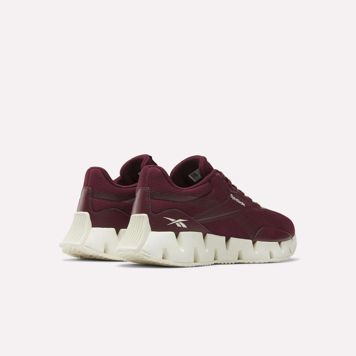 A pair of Women's Zig Dynamica STR Shoes by Reebok in maroon, featuring breathable mesh uppers and chunky white zigzag soles, displayed at an angle on a plain white background.