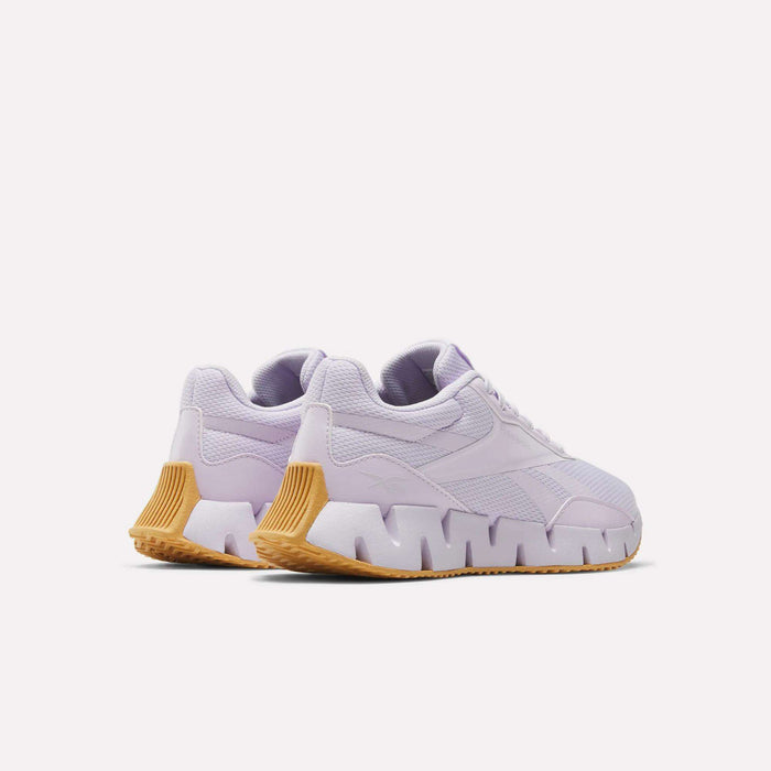 The Reebok Women's Zig Dynamica STR Shoes feature a light purple design with chunky jagged white midsoles, textured tan outsoles, and breathable mesh for comfort, shown on a plain white background.