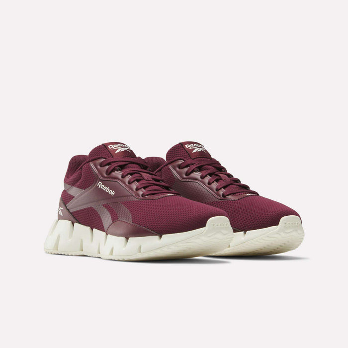 A pair of maroon Reebok Women's Zig Dynamica STR Shoes with white soles, breathable mesh for comfort, and the Reebok logo on the side and tongue, displayed against a plain white background.