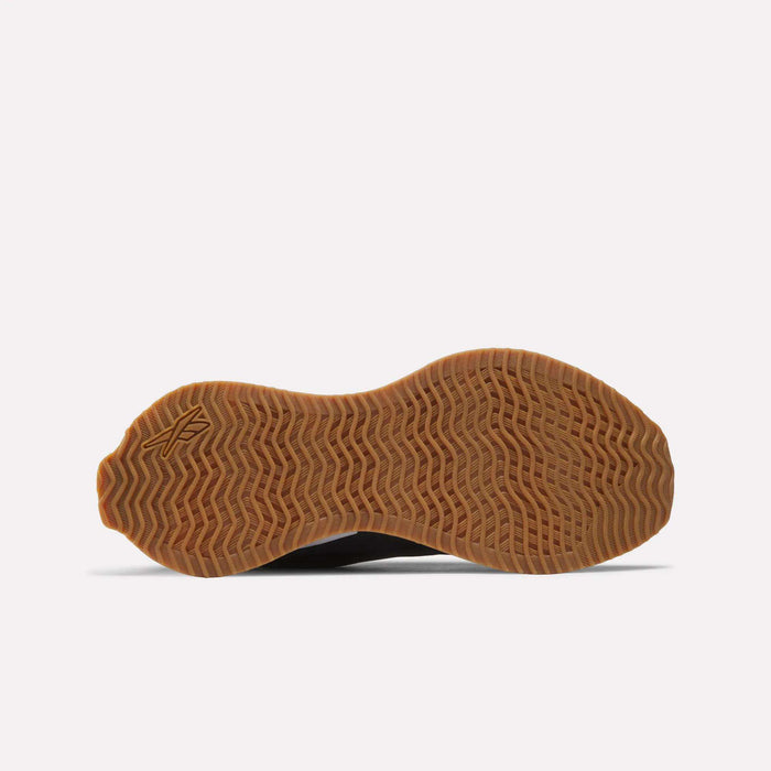 The image displays the brown, wavy-patterned innovative outsole of the Reebok Women's Zig Dynamica STR Shoes, viewed from below on a plain white background. A small stylized A logo is seen on the sole near the heel.