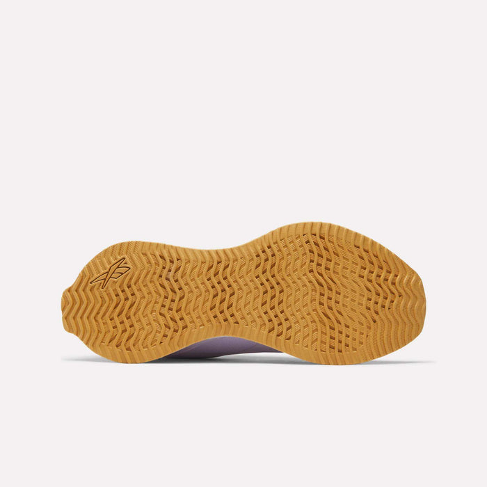 The image shows the bottom view of Reebok Women's Zig Dynamica STR Shoes, featuring a light brown rubber sole with a wavy, textured tread for grip, a small geometric logo near the heel, and reliable EVA cushioning.